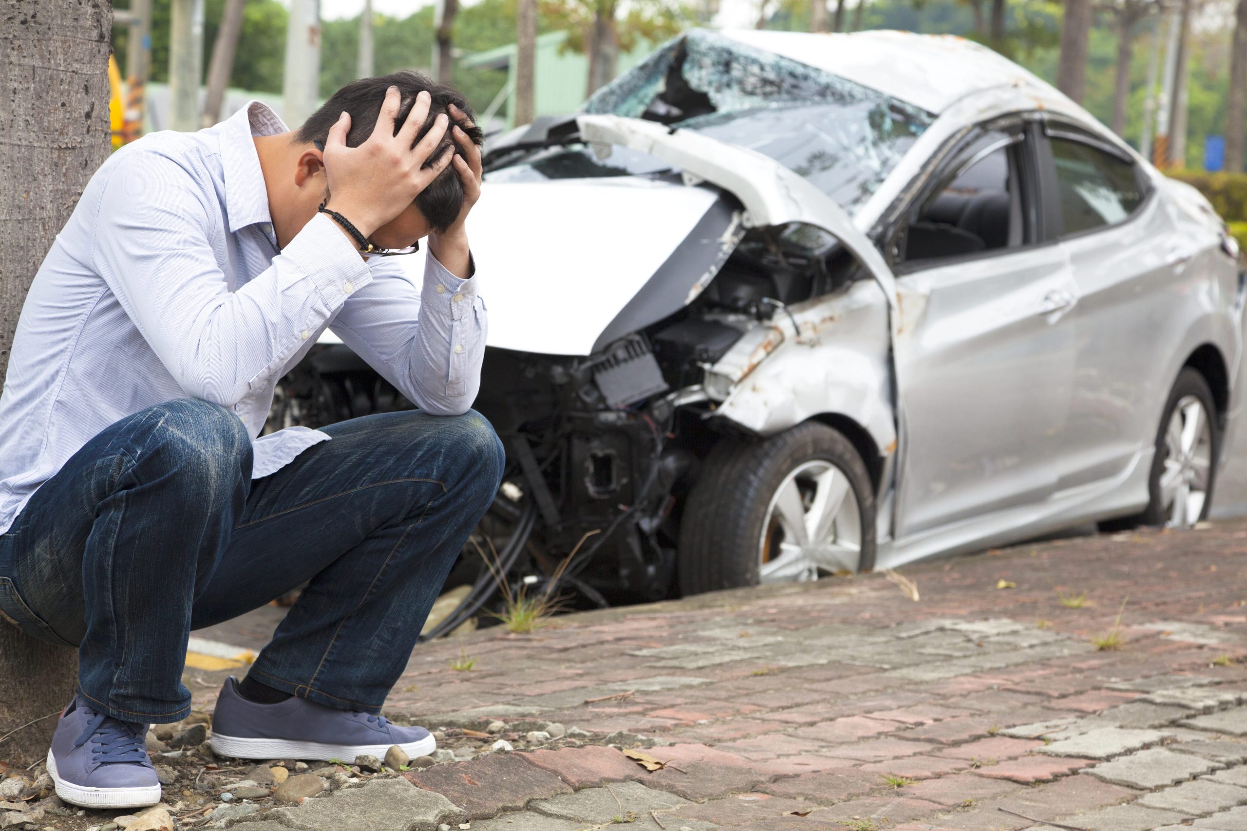 PTSD, man leaning against tree with hands on head, car crash in background