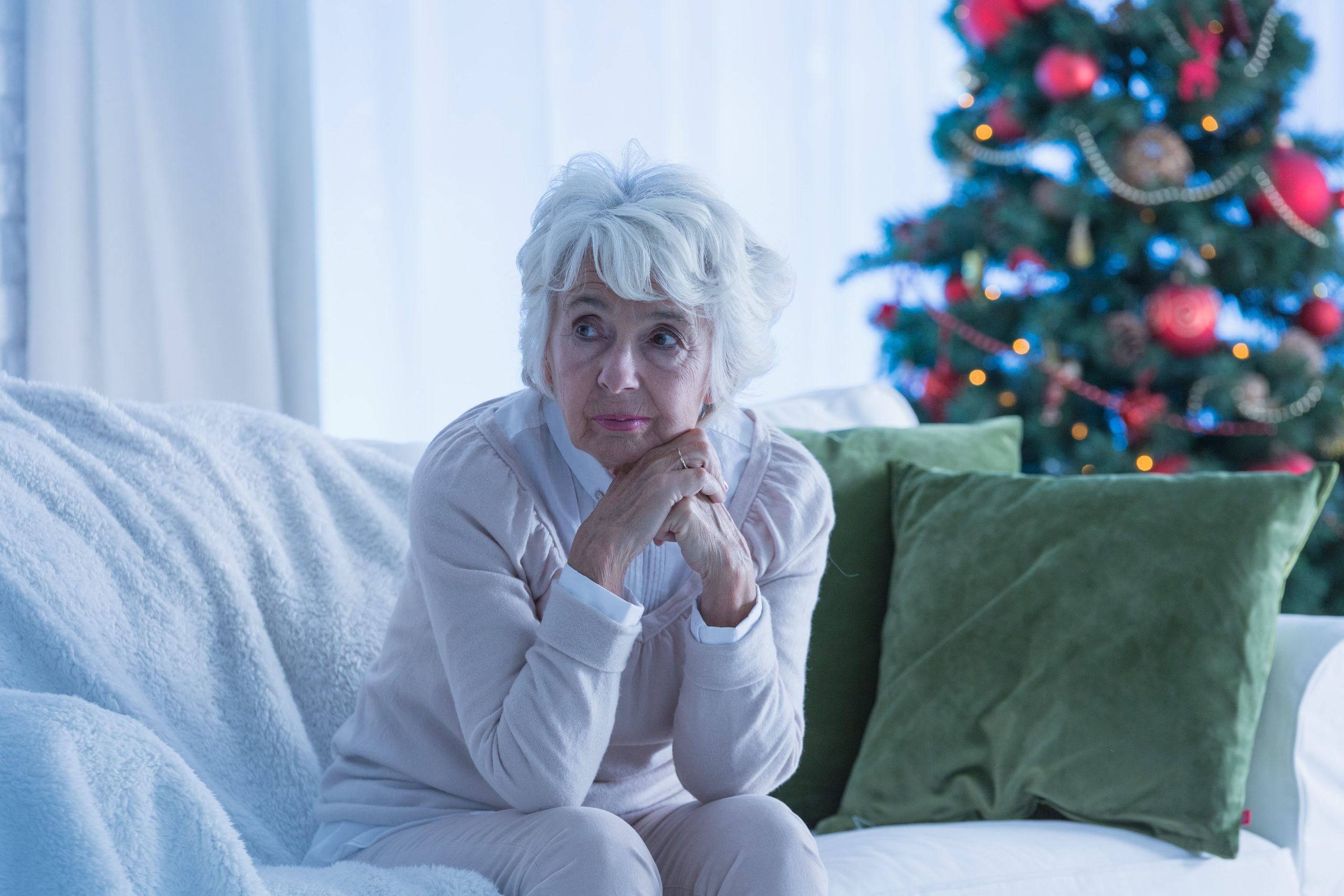 loneliness at Christmas. Elderly lady sitting on chair alone in front of xmas tree.