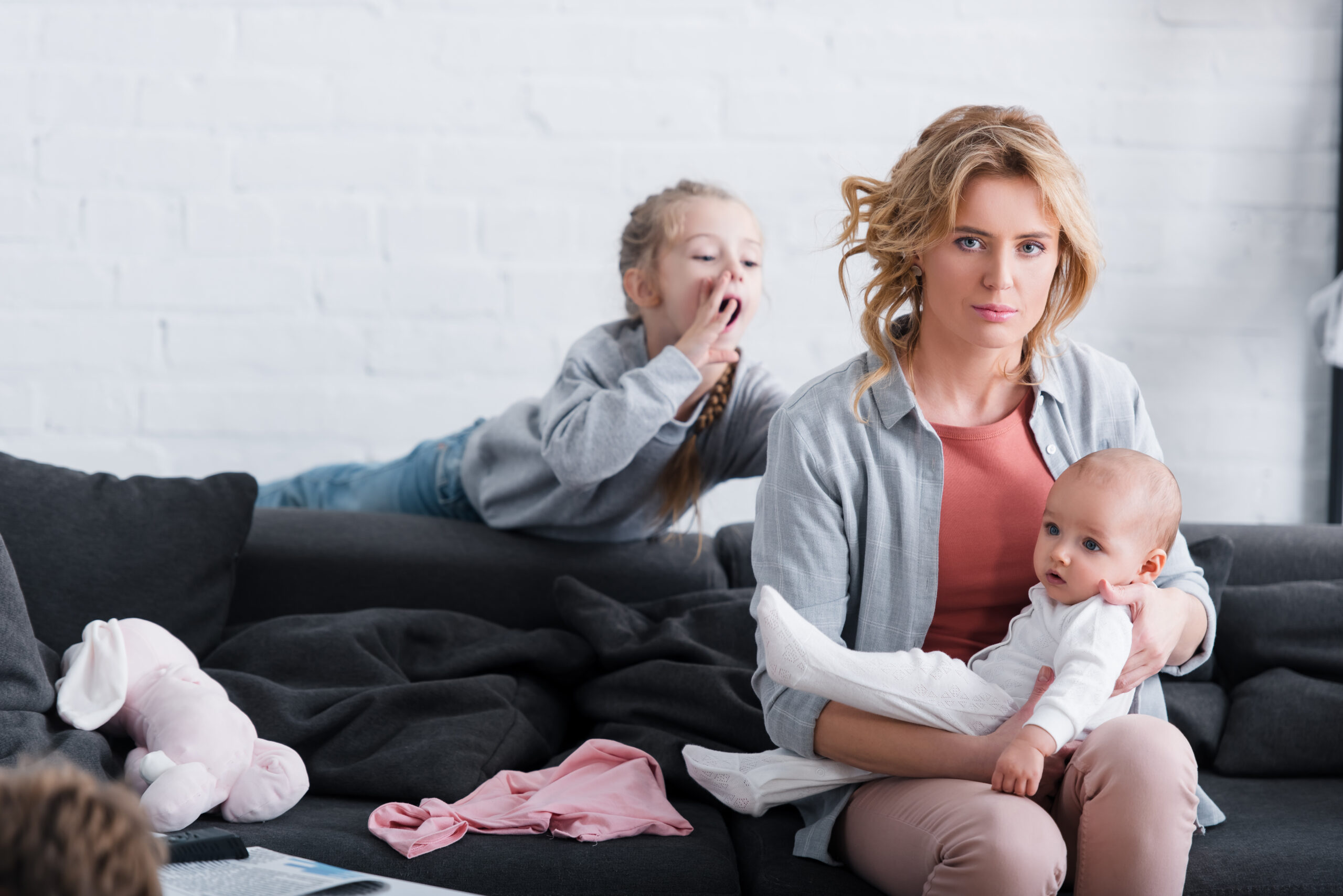 Maternal mental health, mother sitting holding baby with toddler yelling at her from behind