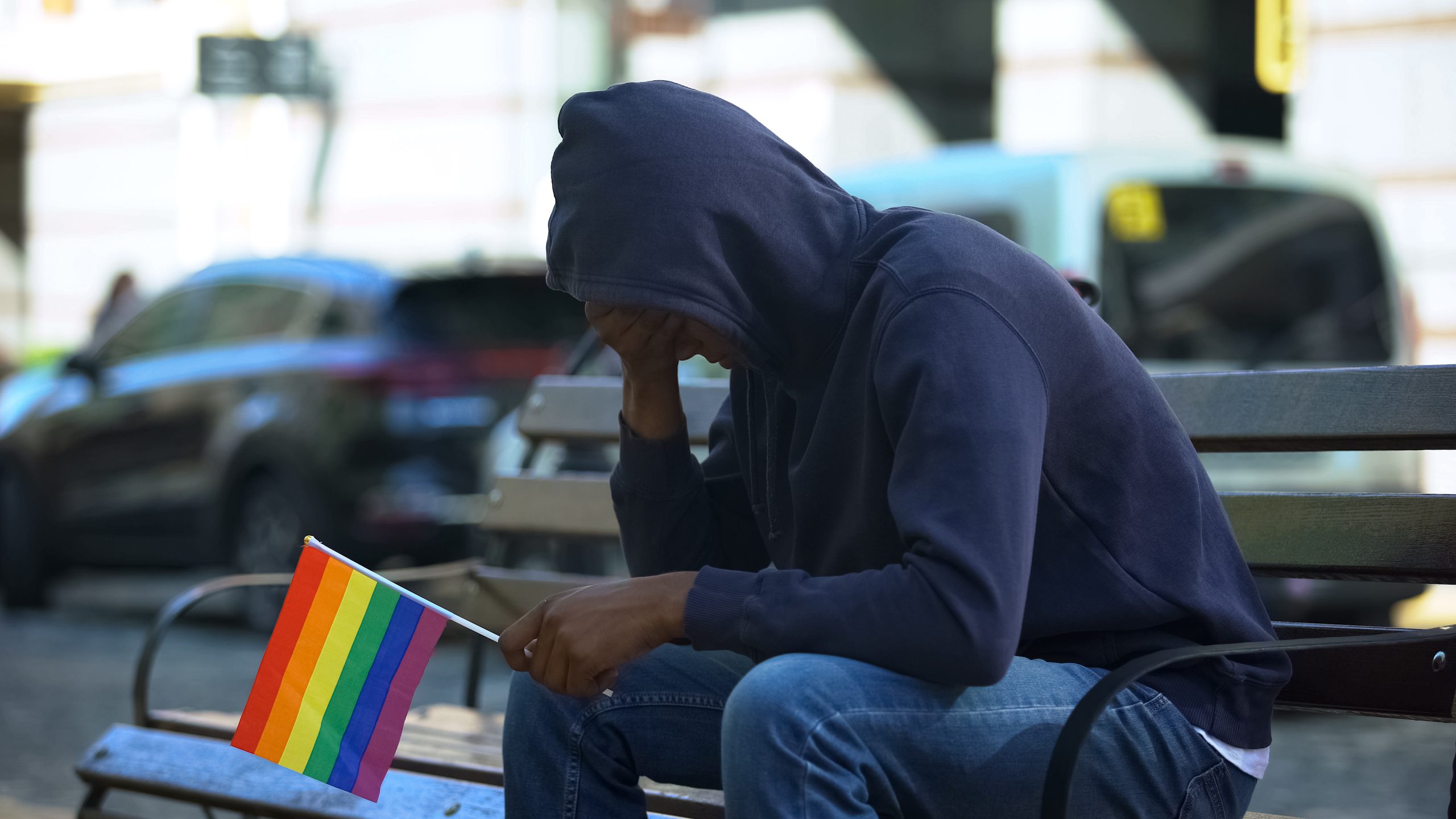 Navigating Sexual Orientation and Mental Health 3 coming out - worried man sitting on bench holding rainbow flag