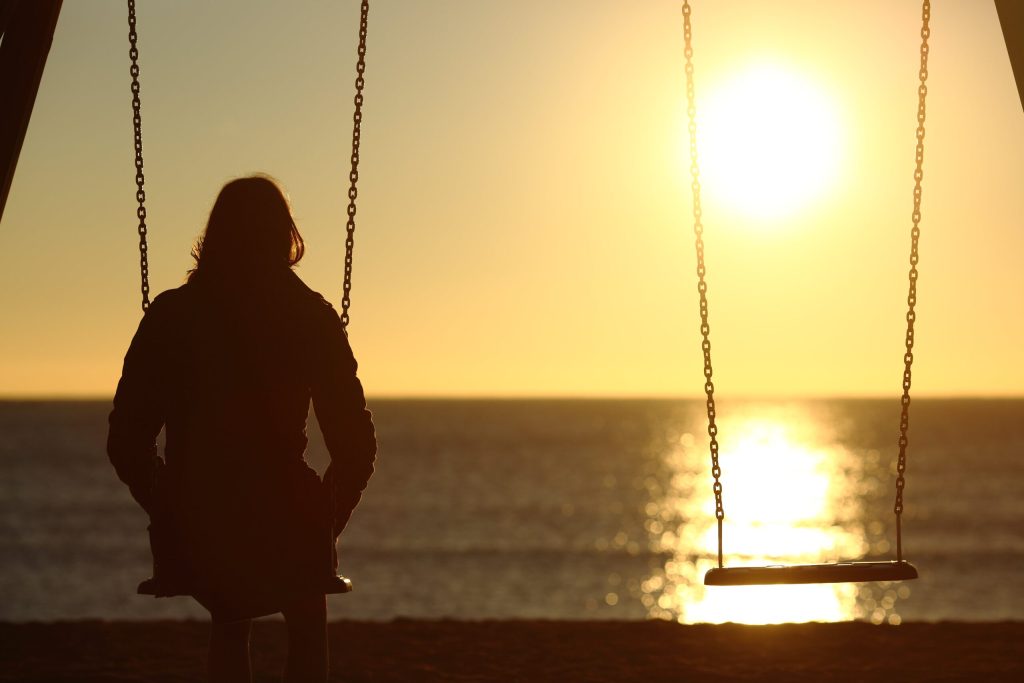 How to Deal with Loneliness for Better Mental Health 12 Loneliness and mental health. Woman sitting on swing at sunset with empty swing next to her.