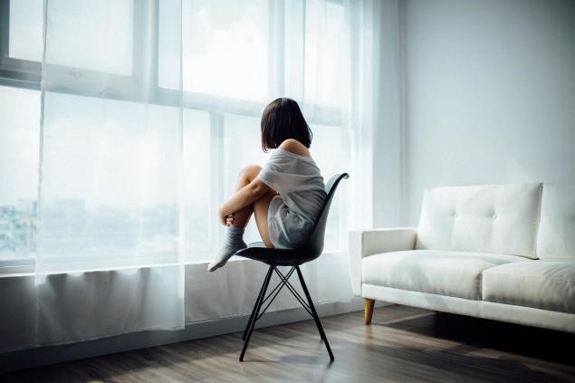 girl sitting on chair looking out window, coping with loneliness