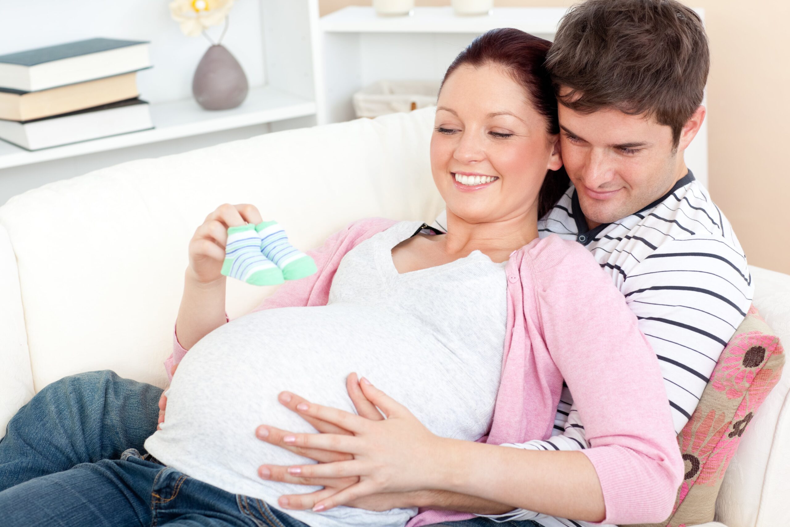 pregnancy mental health, pregnant woman being supported by male partner and looking at baby booties