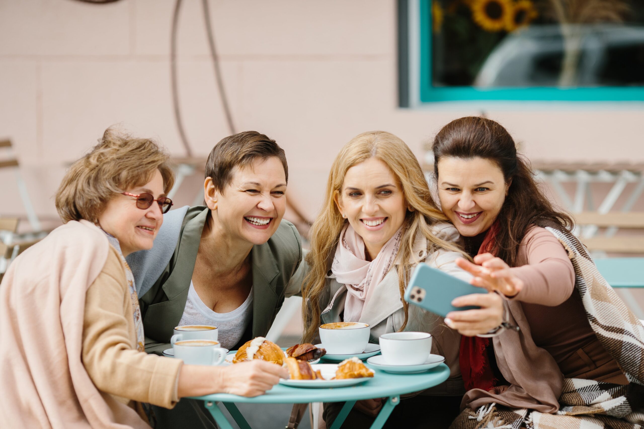 Social isolation and the benefits of connection. Four middle aged women, happy, chatting over coffee at a cafe.